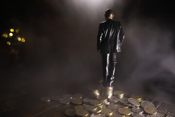 A miniature man standing in front of two paths with a stack of coins of different heights.