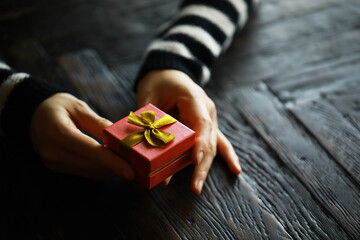Top view of male and female hands holding gift box with ribbon on wooden background. Present for...