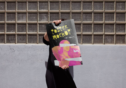 Mockup of man holding customizable A2 vertical poster in front of face by wall