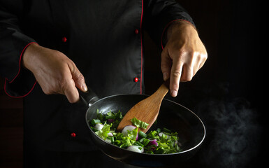 The chef prepares vegetables in a frying pan for a delicious lunch. Place for advertising a hotel or restaurant on a black background. Vegetarian food cooking concept