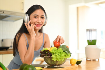 Attractive sportswoman in headphone preparing ingredients for making healthy drink in the kitchen