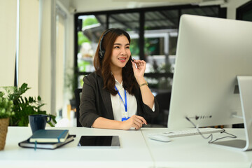 Fototapeta premium Charming asian female call center operator with headset working on support hotline in modern office