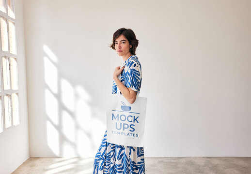 Mockup of woman holding customizable tote bag and looking at camera, side view
