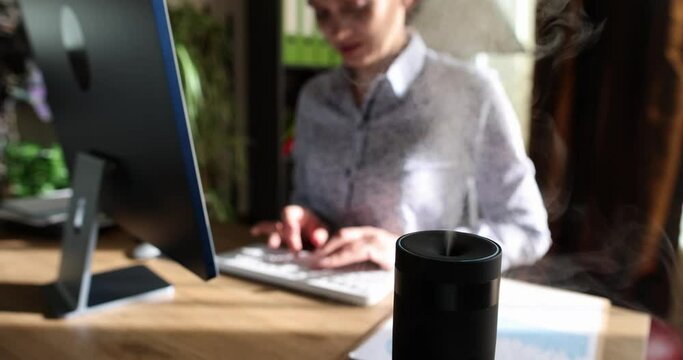 Modern air humidifier device on office desktop. Woman enjoying the aroma of aromatherapy steam from an essential oil diffuser
