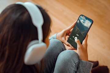 Woman with headphones holding mobile phone listening to music while sitting on the the sofa in living room at homes, Smiling girl relaxing with earphones in morning, Time to relax