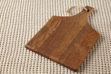 A wooden brown cutting board against a background of a beige coarse knitted blanket. High angle view with copy space