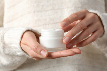 A jar of hand cream in hands on a light background.