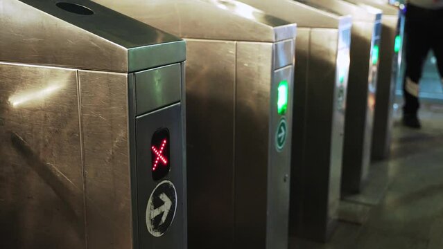 Close up of people go through turnstiles at night on the tram metro station. Red light change to green after payment