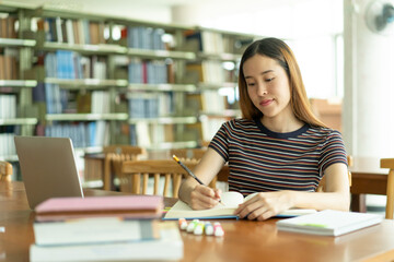 Female asian student studying and reading book in library