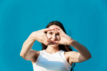 very beautiful young adult woman brunette with long hair in white tight t-shirt with hands making...