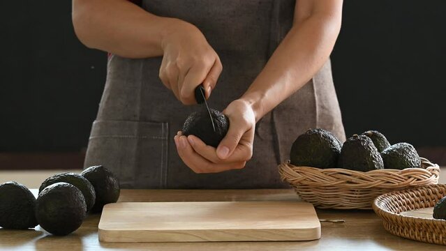 Ripe hass avocado fruit with hand holding knife and cutting
