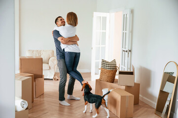 Man is holding woman in hands, happiness. Young couple with dog are moving to new home