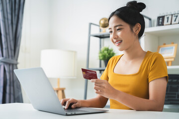 Young Asian woman holding credit card and using laptop for shopping online with payment on internet...