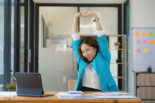 Young Asian businesswoman stretching arms raised relaxing at the office.