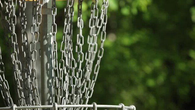 Close up of a frisbee going in to a frisbeegolf basket in slow motion