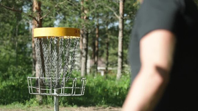 Person throwing a frisbee to a frisbeegolf basket in slow motion