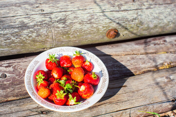 Close-up strawberry crop lying in a plate on rural wooden steps. The concept of healthy food, vitamins, agriculture, market, strawberry sale