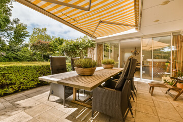 an outdoor dining area with table and chairs under the awning on a sunny day in the patio is surrounded by lush green trees - obrazy, fototapety, plakaty