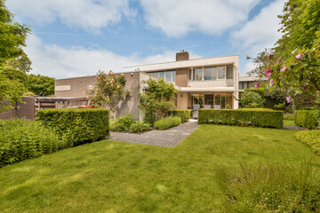 a house in the middle of a green yard with bushes and flowers on either side of the house there is a blue sky above
