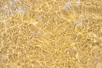 Top view of transparent clean water of sea ocean. Yellow sand seen through water. Sun rays reflecting on waves. Summer.