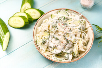 Salad of kohlrabi and fresh cucumber in sour cream sauce with tarragon. Salad in white bowl on blue wooden background. Keto.