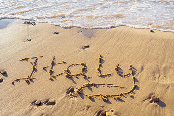 Close-up of inscription word Italy written on sand of beach seashore coastline after tide near sea waves on sunny day.