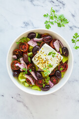 Bowl of traditional Greek salad with tomatoes, cucumbers, red onions, kalamata olives, feta sheep cheese and olive oil.