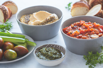 Vegetarian appetizers: hummus, roasted peppers salad, pesto and fresh vegetables.