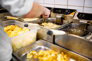 Chef cooking delicious potato chips in hot oil on kitchen