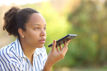 Black woman dictating text on phone in a garden