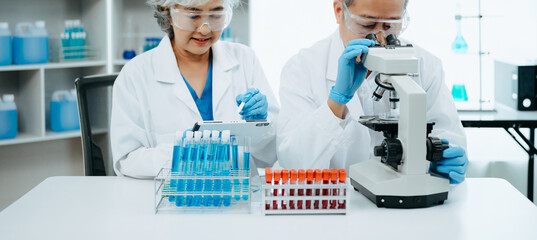 Fototapeta premium Two scientist or medical technician working, having a medical discuss meeting with Asian senior female scientist supervisor in the laboratory with online reading, test samples and innovation