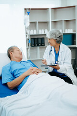 Obraz premium Friendly Female Head Nurse Making Rounds does Checkup on Patient Resting in Bed. She Checks tablet while Man Fully Recovering after Successful Surgery in hospital