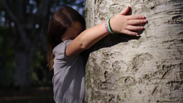 Little girl embracing tree in the forest. Environmental education concept