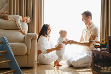 Family with two kids on the couch having fun. Mather, father baby and toddler sons are happy in the morning in Livingroom. Children playing with parents at home. Learning to walk, first steps