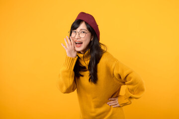 Happy young Asian woman wearing yellow sweater with open mouths raising hands screaming announcement isolated on yellow background