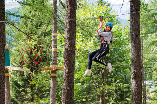 Happy young woman having fun on ropes in forest adventure park