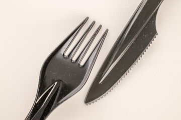 One plastic knife and fork on a white ceramic plate, macro, top view.