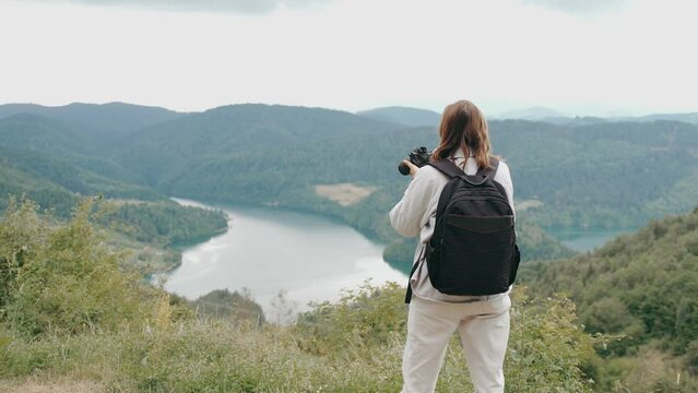 A woman professional photographer takes a picture of a beautiful landscape standing on a hill overlooking the lake