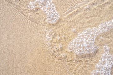 Top view of clear foamy water of sea ocean. Yellow golden clean sand seen through water. Beach, summer, holidays, sea.
