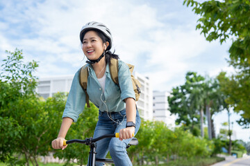 Happy Asian woman wearing a helmet and listening to her favorite music while riding a bicycle...