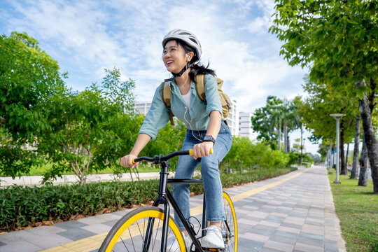 Happy young Asian woman while riding a bicycle in a city park. She smiled using the bicycle of transportation. Environmentally friendly concept.
