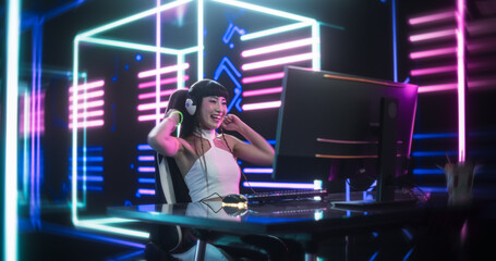Fototapeta na wymiar Internet Streamer Making a Live Video Game Broadcast on Social Media Channels. Asian Girl Using a Desktop Computer in a Room with Futuristic Neon Background. Gamer Winning and Celebrating