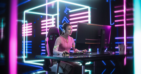 Fototapeta na wymiar Young Female Gamer Playing Online Video Game on Computer. Portrait of an Excited Woman in Headphones Battling in PvP Tournament with Other Players, Talking with Team on Microphone