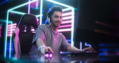 Fototapeta na wymiar Portrait of a Young Man Putting On Headphones, Talking with Teammates Online During an Intense Computer Match. Streamer or Gamer Playing and Chatting with Internet Followers in a Futuristic Neon Room