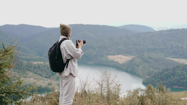 A female photographer enjoys a beautiful view of the lake standing on a hill during her autumn trip
