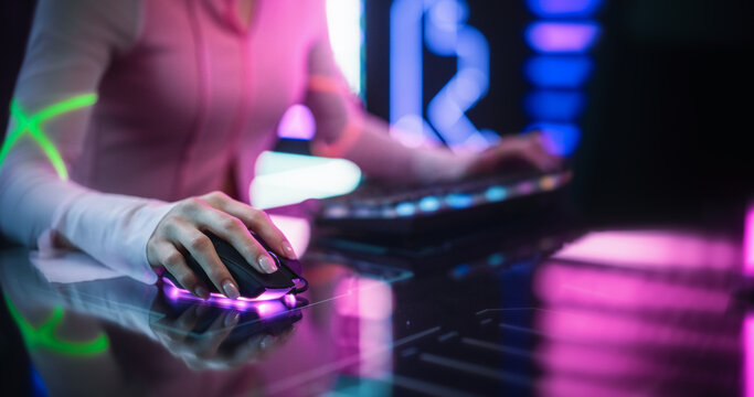 Close Up of a Female Gamer Girl Playing on a Computer. Focus on Hands Using Keyboard and Mouse. Streamer Sitting Behind a Futuristic Interactive Desk in a Colorful Neon Studio Room