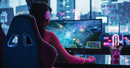 Young Female Gamer Playing Online Multiplayer Battle Arena Video Game on a Computer in a Cyberpunk Digital Neon Studio. Asian Girl Using a Modern Wide Curved Monitor for Her Gaming Station Setup © Gorodenkoff