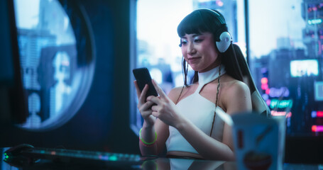 Beautiful Smiling Asian Female Using Smartphone while Sitting Behind a Desk in a Futuristic...