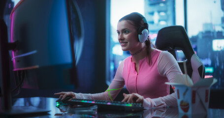 Fototapeta na wymiar Young Woman Wearing Futuristic Clothes, Bright Green Makeup and Neon Rings, Playing Video Games on a Desktop Computer. Beautiful Girl Participating in a Cybersport Tournament from Her Futuristic Home