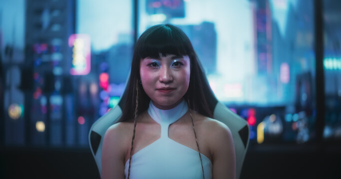 Medium Portrait of a Beautiful Japanese Looking at the Camera and Smiling in a Technologically Advanced Room with Futuristic Cyberpunk City in the Background. Female Sitting Behind a Desk